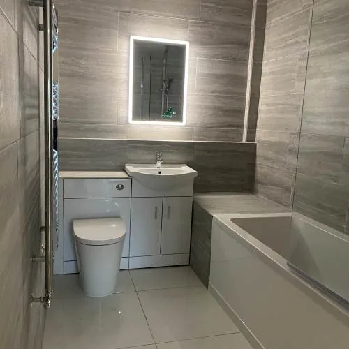 Grey wood-effect tiled bathroom with LED mirror, white vanity unit and bath