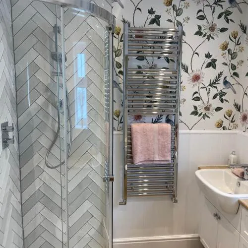 Herringbone tiled shower with chrome towel rail and floral wallpaper