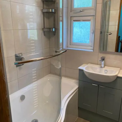 L-shaped shower bath with grey vanity unit and chrome corner shelving