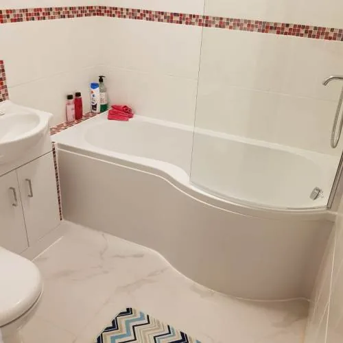 P-shaped shower bath with a red mosaic border tile and white vanity