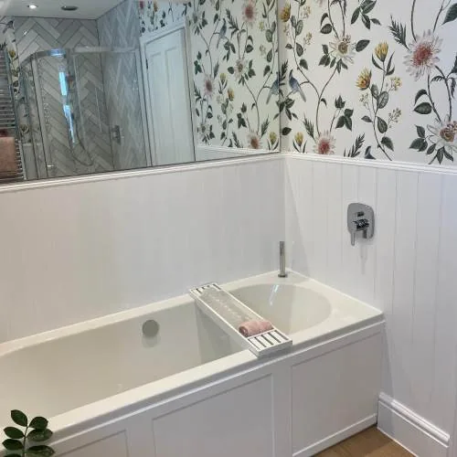 Panelled bath with white wall panelling and floral wallpaper