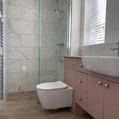 Pink vanity unit with wall-hung toilet and glass shower enclosure