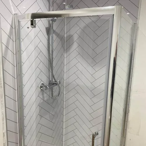 Square shower enclosure with herringbone wall tiles and chrome riser