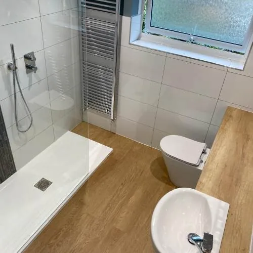 Walk-in shower tray with wood-effect flooring and chrome towel rail