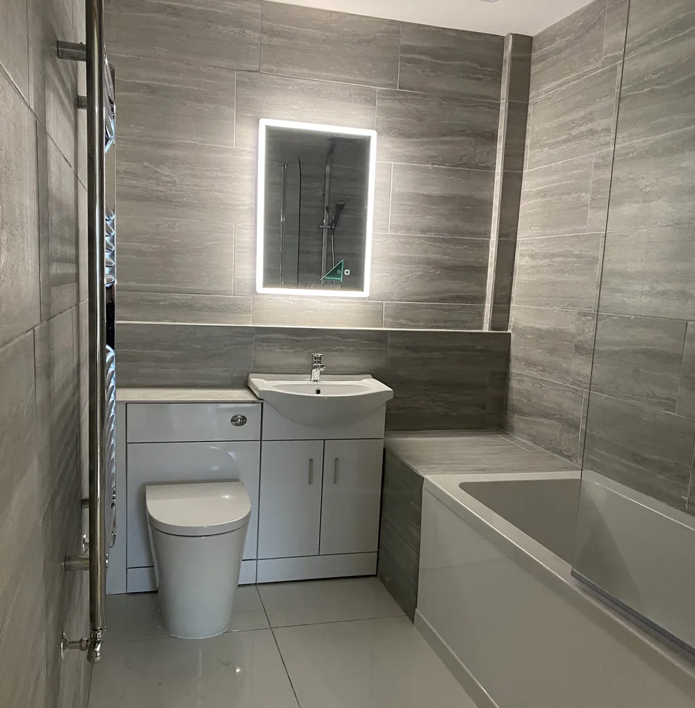 Grey tiled bathroom with LED mirror, vanity unit and bath, fitted as part of our plumbing services in Hampshire